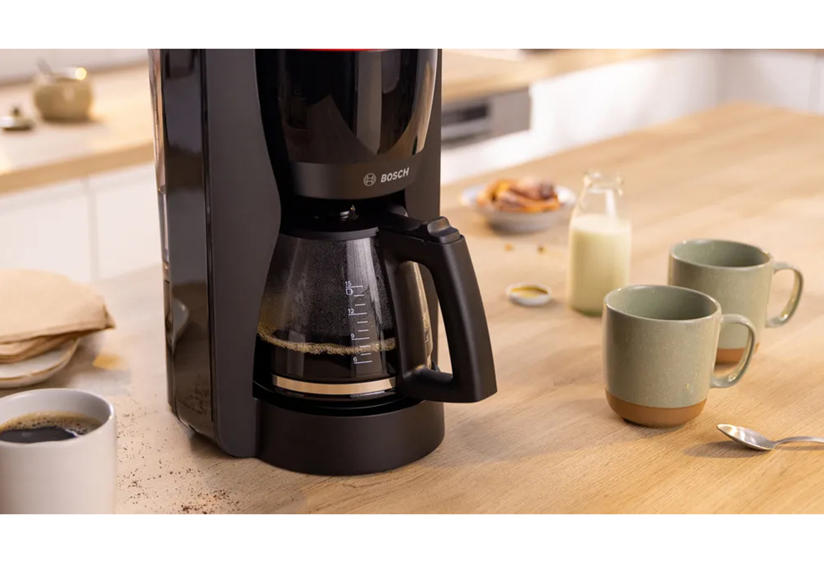 Απεικονίζεται η μηχανή πάνω σε τραπέζι μαζί με κούπες και άλλα σχετικά αντικείμενα.